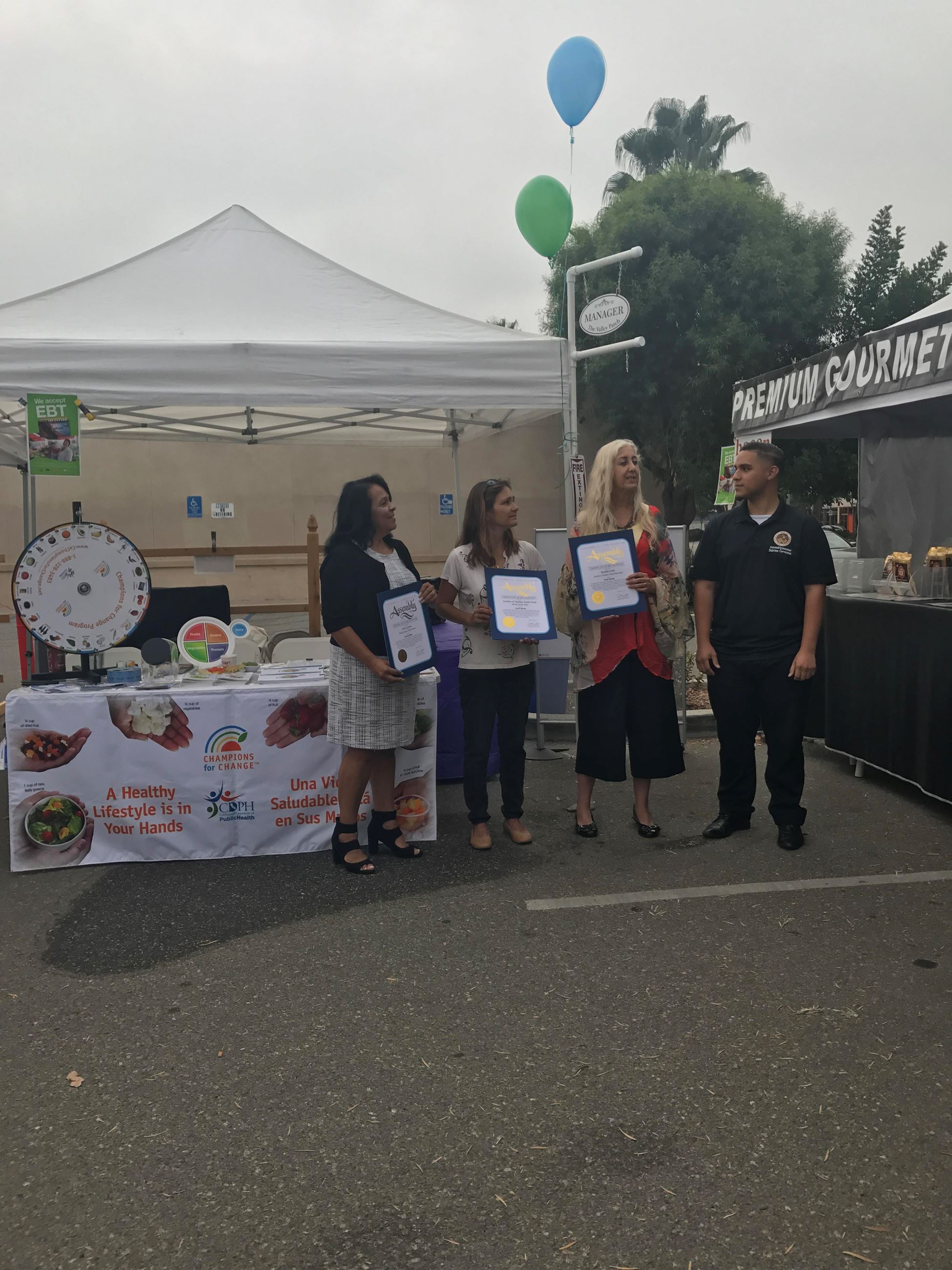 Women Holding Awards Standing Next to Man at Farmer's Market